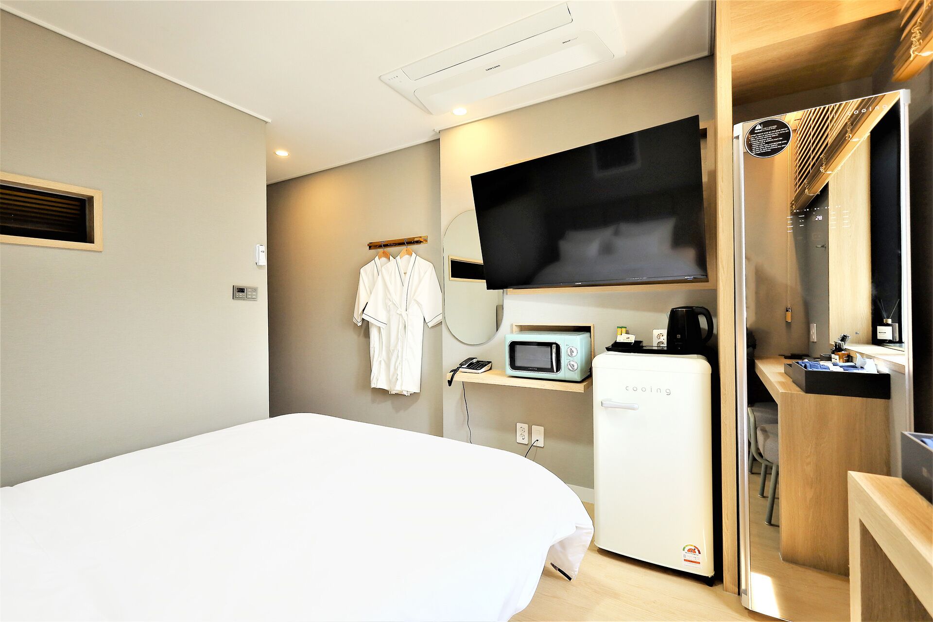 Ein Hotelzimmer mit Bett, Fernseher, Mikrowelle, Minikühlschrank und einem kleinen Schreibtisch mit Kaffeemaschine.