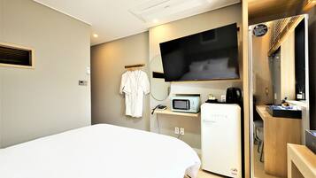 Ein Hotelzimmer mit Bett, Fernseher, Mikrowelle, Minikühlschrank und einem kleinen Schreibtisch mit Kaffeemaschine.