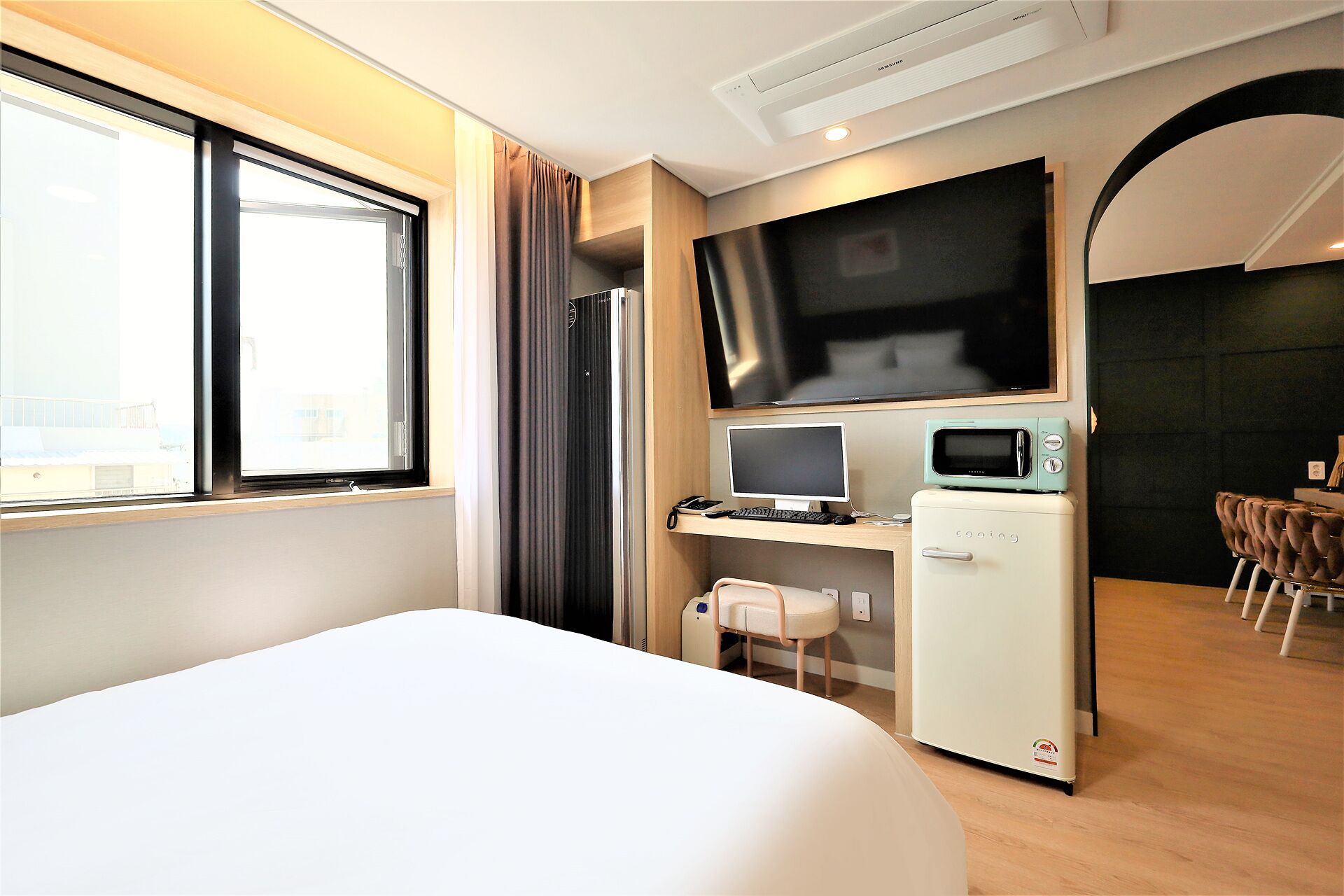Una habitación de hotel con cama, escritorio con computadora y microondas, televisión y ventana con cortinas.