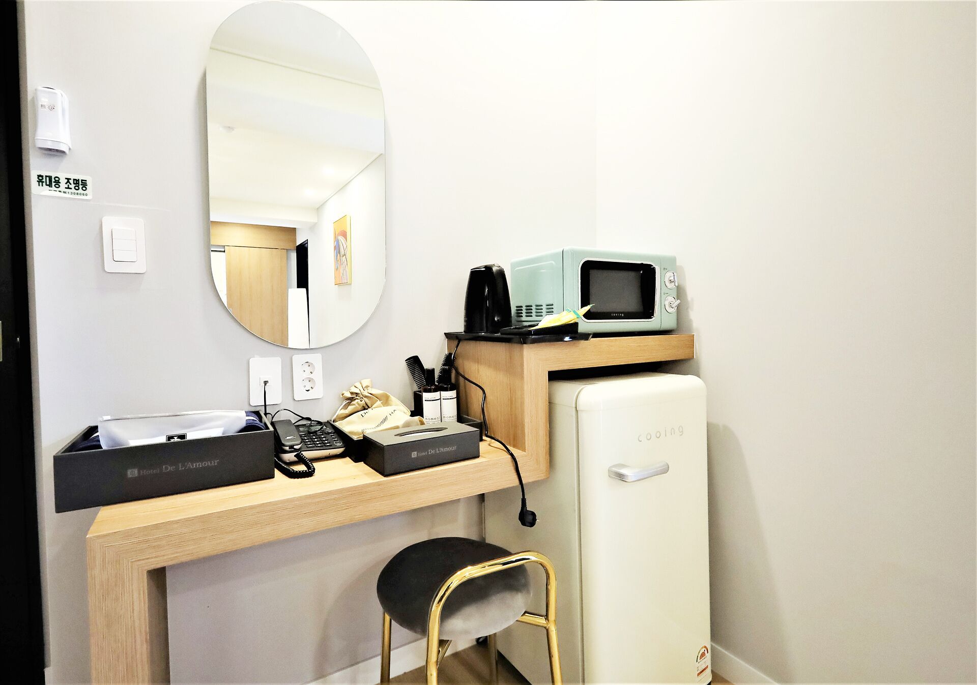 A hotel room with a desk, a microwave, a refrigerator, a chair, and a mirror.