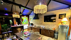 Une cuisine moderne avec des meubles de rangement en bois foncé, un réfrigérateur en acier inoxydable et un coin repas comprenant une table et des chaises en bois.