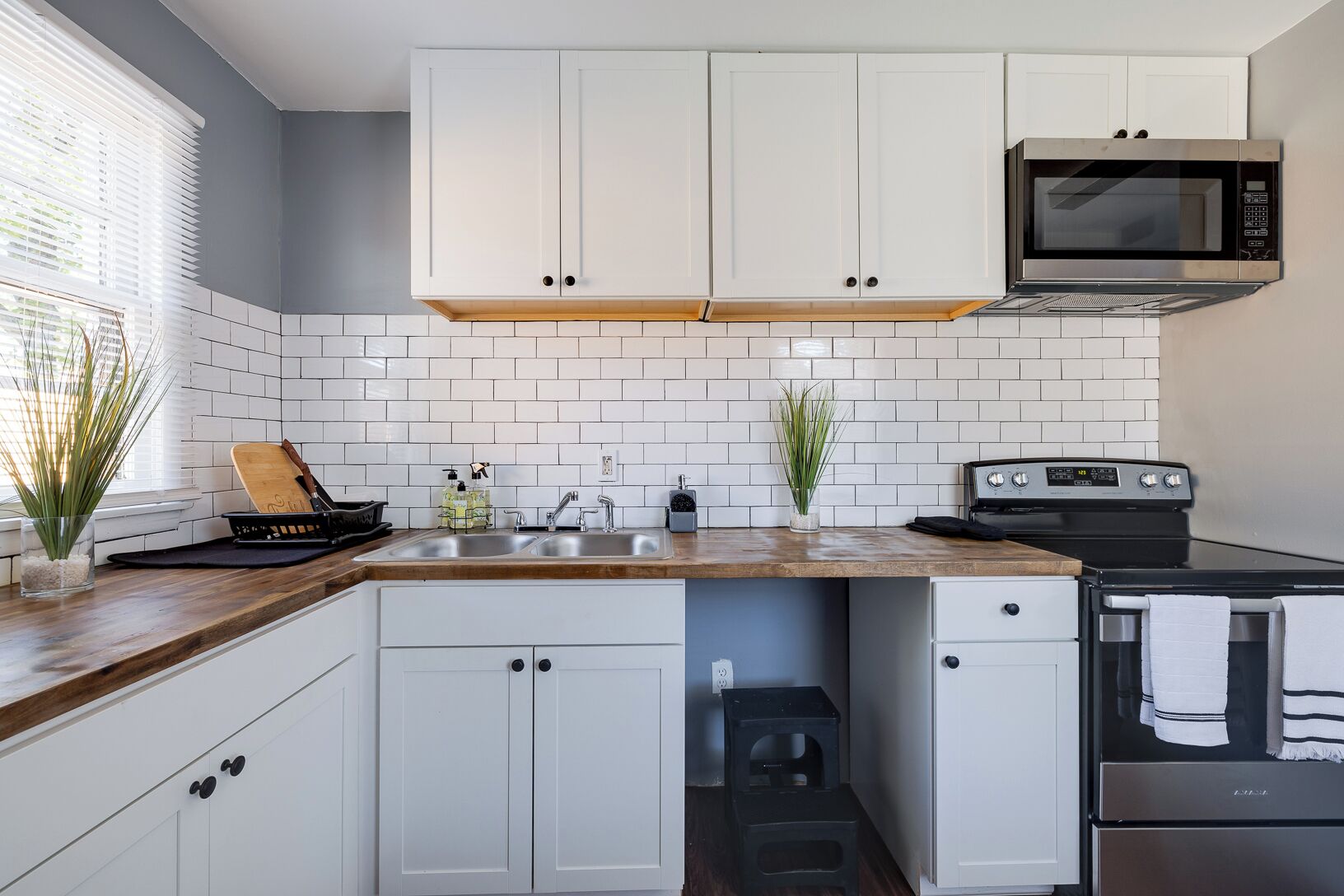 A kitchen with white cabinets, a microwave, a stove, and a sink.