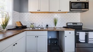 Una cocina con armarios blancos, microondas, estufa y pileta.