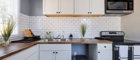 A kitchen with white cabinets, a microwave, a stove, and a sink.