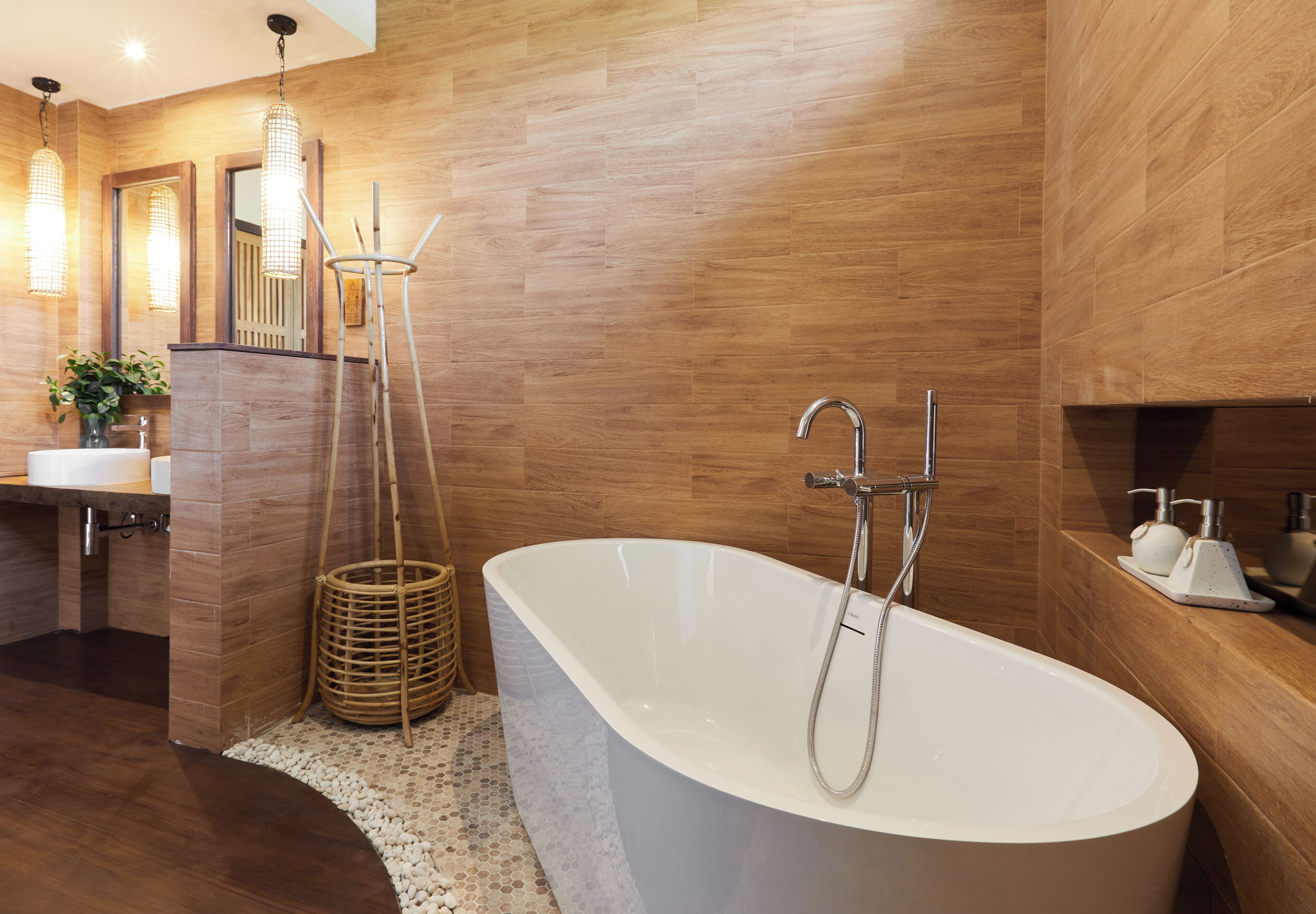 A modern bathroom with a freestanding bathtub, wooden flooring, and a large mirror.