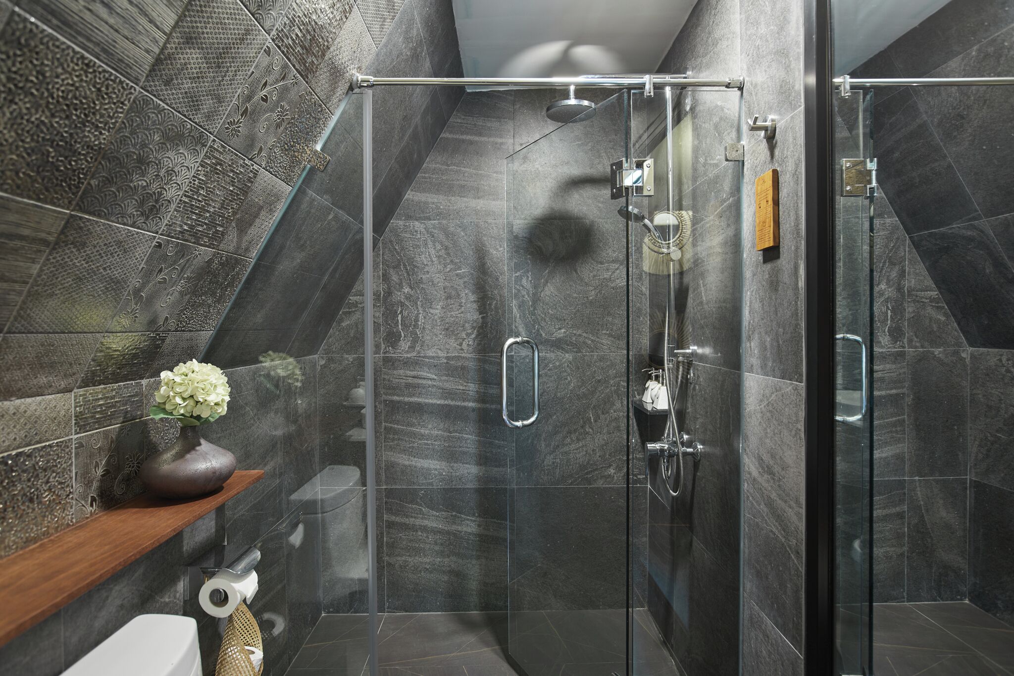 Een moderne badkamer met een douchecabine van glas, donkere marmeren tegels en een houten plankje met een vaas.