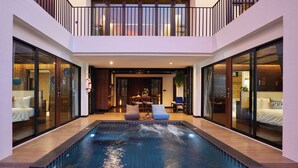 Uma área interna de piscina moderna com barreira de vidro, piso de madeira e um espaço de estar com cadeiras e uma mesa.