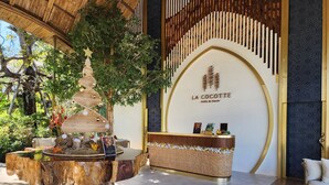Uma área de recepção com um balcão de madeira, uma escultura de árvore decorativa e uma placa com a inscrição "LA COCOTTE Villa & Farm".