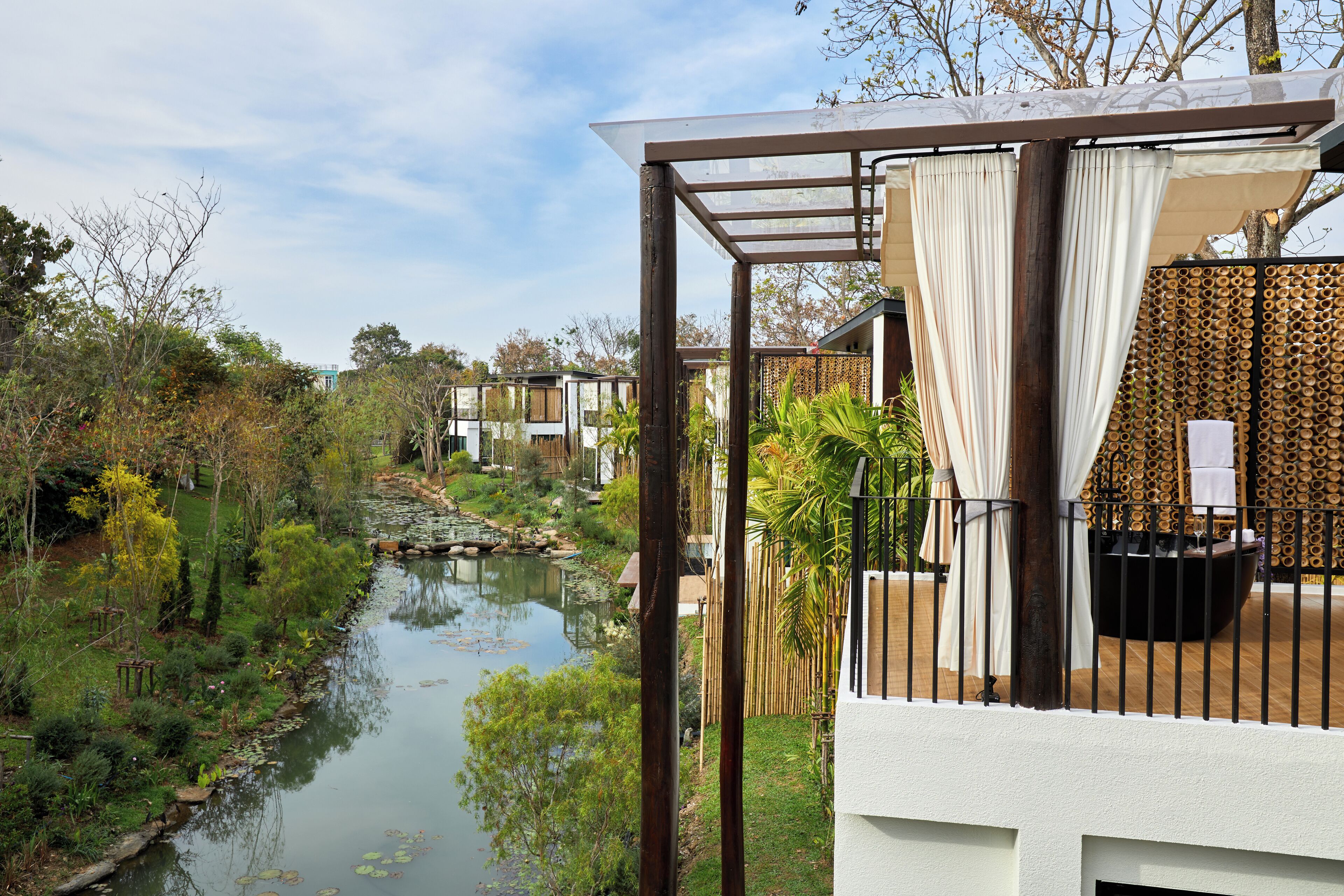 A serene outdoor area with a pond, lush greenery, and a wooden deck with a seating area.