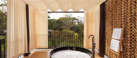 Un jacuzzi negro grande lleno de agua, rodeado de piso de madera y cortinas color beige.