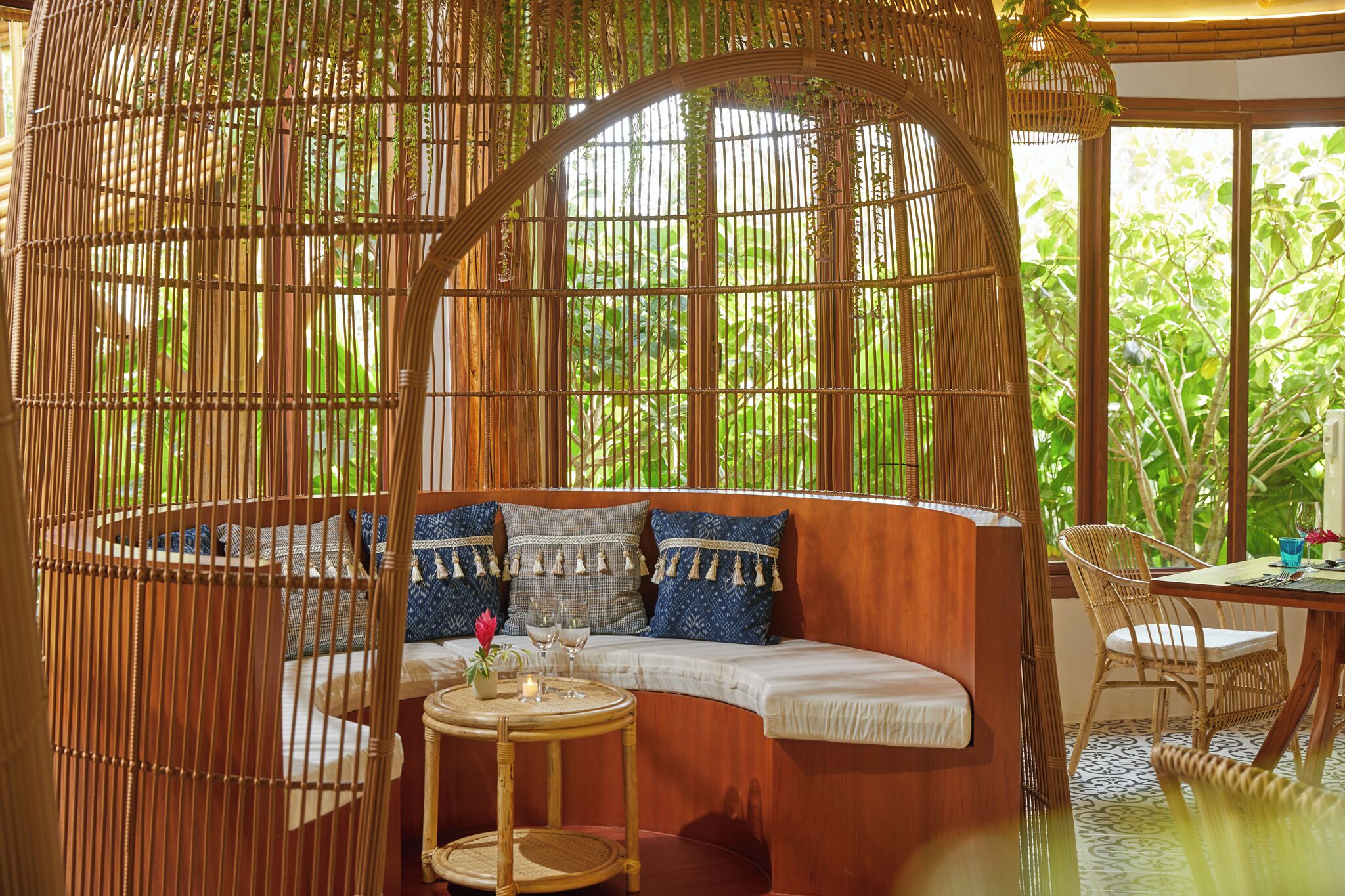 A room with a curved wooden bench, a round table with candles, and a wicker chair.