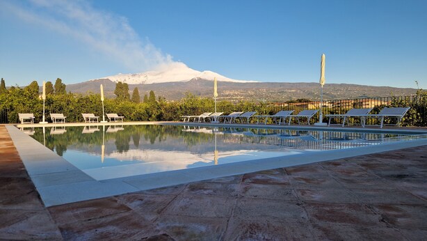 A swimming pool with lounge chairs, a mountain in the background, and a clear sky. - Lumia (Riposto)