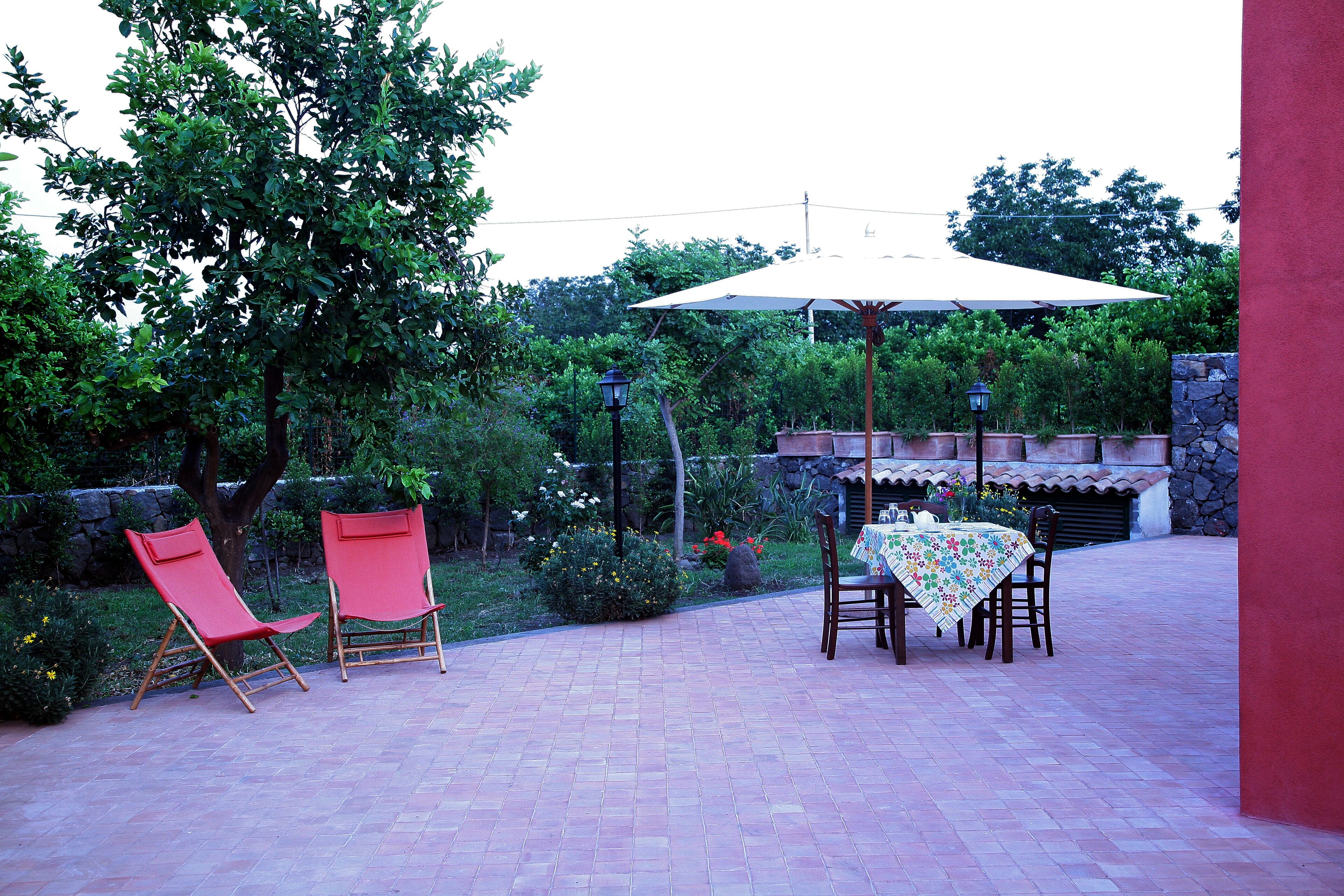 An outdoor patio with a table and chairs, surrounded by greenery and a stone wall.