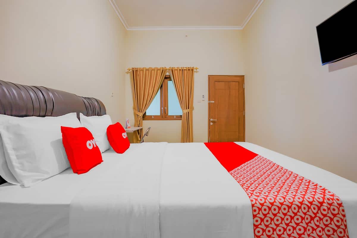 A hotel room with a bed, red and white bedding, a wooden door, and a TV mounted on the wall.