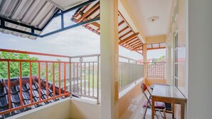 A balcony with a metal railing, a table with chairs, and a view of a red-roofed building. - Hotel O Kenari House Syariah (Depok)