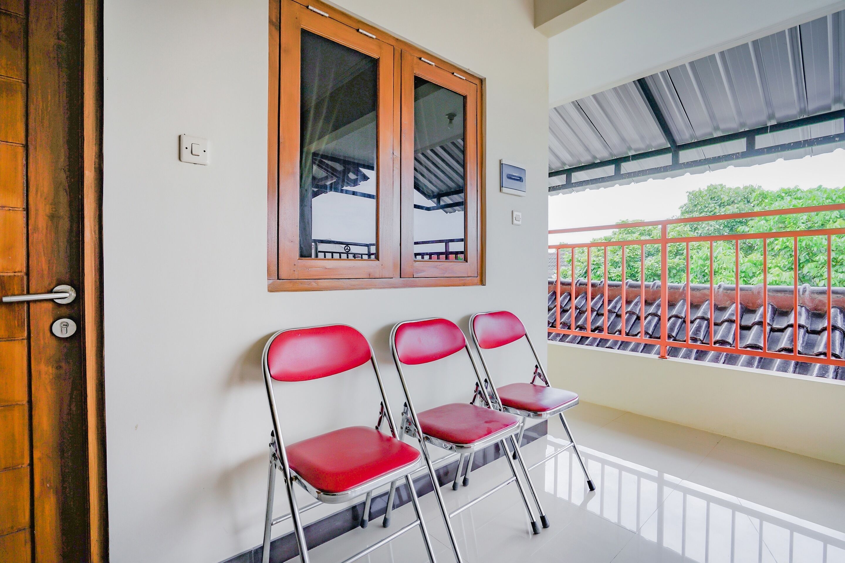 A room with a wooden door, a window with a metal frame, and a balcony with a red railing.