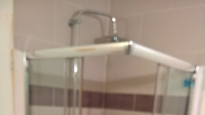 Eine begehbare Dusche mit Glaswänden, Fliesen und einer Metall-Duschbrause.