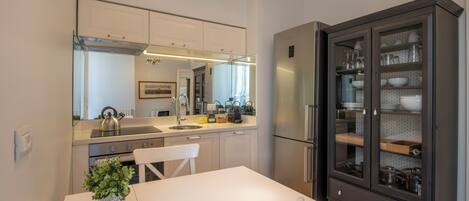 A modern kitchen with white cabinets, a stainless steel refrigerator, and a dark wooden cabinet with glass doors.