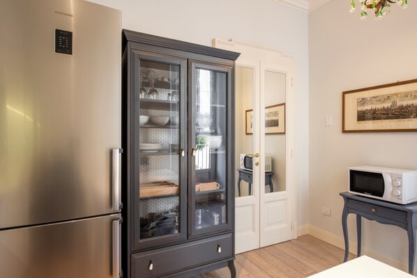 A kitchen with a stainless steel refrigerator, a dark wooden cabinet with glass doors, and a microwave on a small table.