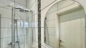 Un baño con ducha de vidrio, pared con azulejos y un espejo grande.