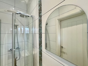 A bathroom with a glass-enclosed shower, a tiled wall, and a large mirror.
