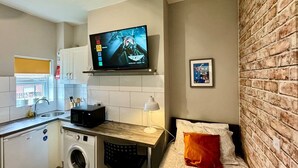 Habitación pequeña con cama, lavadora, microondas, lavabo y televisor sobre el mostrador.