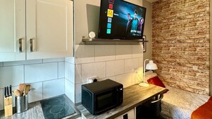 Una cocina moderna con armarios blancos, microondas, televisor montado en una pared de ladrillo y encimera de madera.
