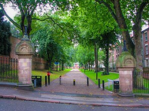 A tree-lined pathway leading to a building with a brick facade.
