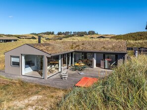 A modern house with a glass-enclosed patio area, a deck, and a view of the surrounding landscape.