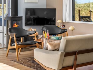 Un salon moderne avec une cheminée, un canapé, un téléviseur et une fenêtre donnant sur l’extérieur.
