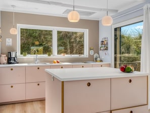 A modern kitchen with a large window, pendant lights, and a view of greenery outside.