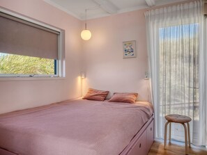 A single bed with a pink bedspread and two pillows, a window with a view of greenery, a wall-mounted light, and a small stool. - "Hoat" - 300m from the sea by Interhome (Saltum)