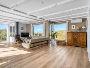 A spacious living room with a sofa, TV, and large windows overlooking a natural landscape.
