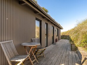 A wooden deck with two chairs and a table, a building with vertical siding, and a clear sky.