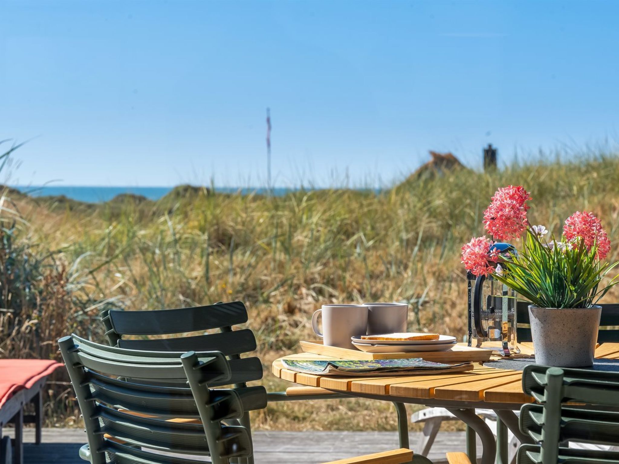 An outdoor dining area with a table, chairs, a potted plant, and a view of the beach.