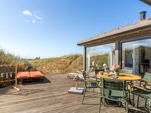 A wooden deck with outdoor furniture, a glass-enclosed room, and a view of the landscape.