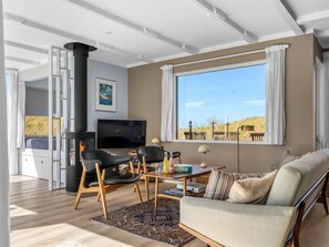 A modern living room with a fireplace, a sofa, a TV, and a large window offering a view of the outdoors. - "Hoat" - 300m from the sea by Interhome (Saltum)