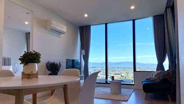 Una sala de estar moderna con comedor, ventanas amplias y vistas a un paisaje urbano.