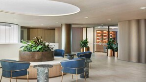 Un vestíbulo moderno con mostrador de recepción, sillas azules, una mesa redonda y una decoración de plantas.