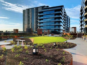 A modern building with multiple balconies, a central courtyard with grass and seating, and a clear sky.