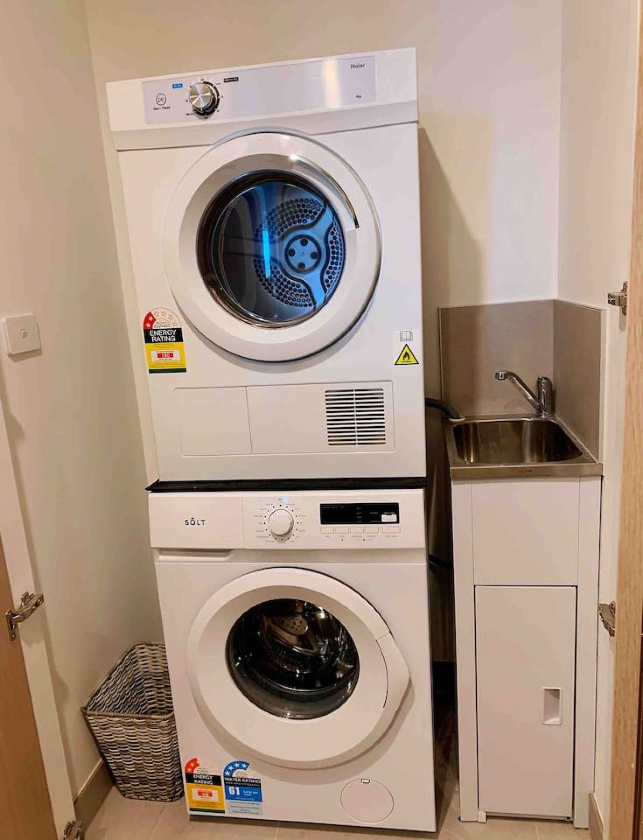 A stacked washer and dryer unit with a small sink and cabinet.