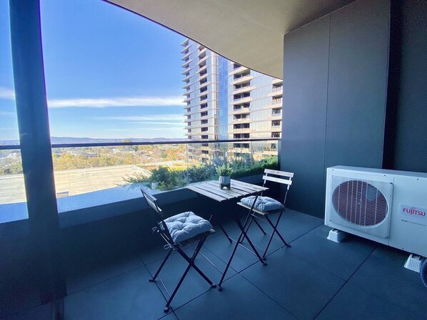 A balcony with a table and chairs, a potted plant, and an air conditioning unit.