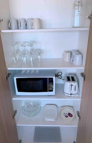 A kitchen with a microwave, toaster, and various glassware and dishes.