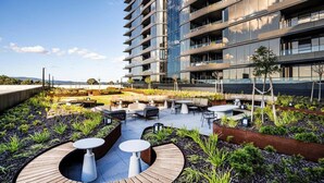 Un jardín en la azotea con mobiliario exterior y un edificio moderno al fondo.