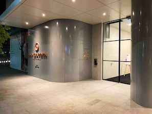 A modern building entrance with a curved facade, a glass door, and a sign indicating the address. - SkyGarden Lux Apt | Sunrise View | Pool/Parking (Glen Waverley)