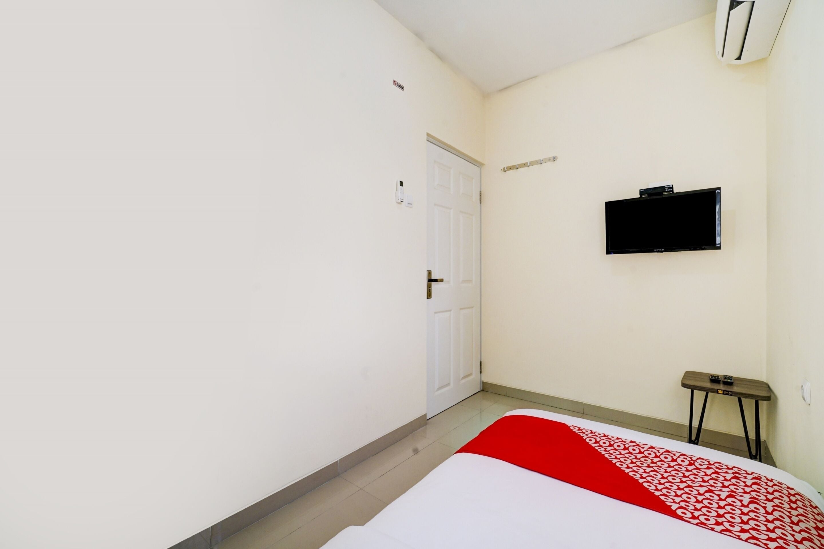 Habitación de hotel con cama, televisor montado en la pared, puerta y una mesita.