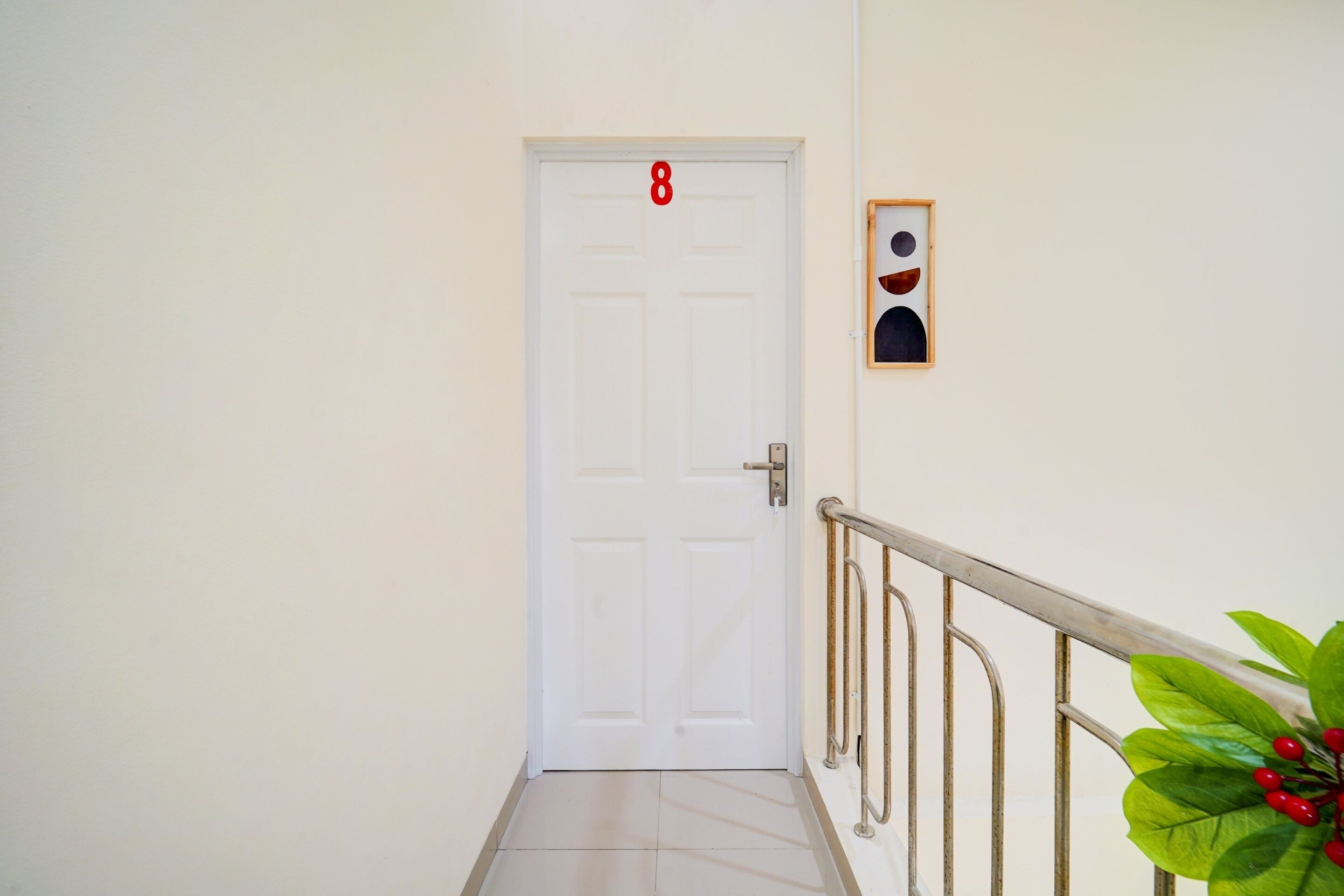 A white door with the number 8, a metal handrail, and a framed picture on the wall.