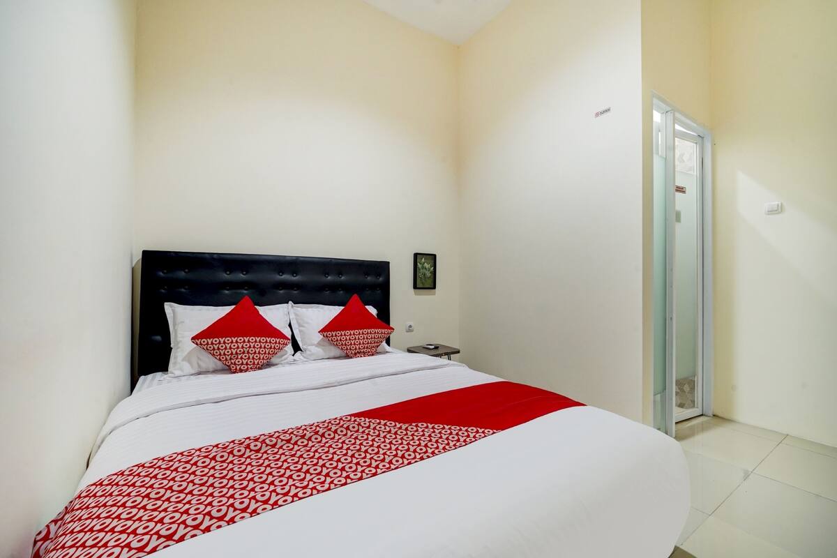 A neatly made bed with a red and white patterned bedspread, a black upholstered headboard, and two red pillows.
