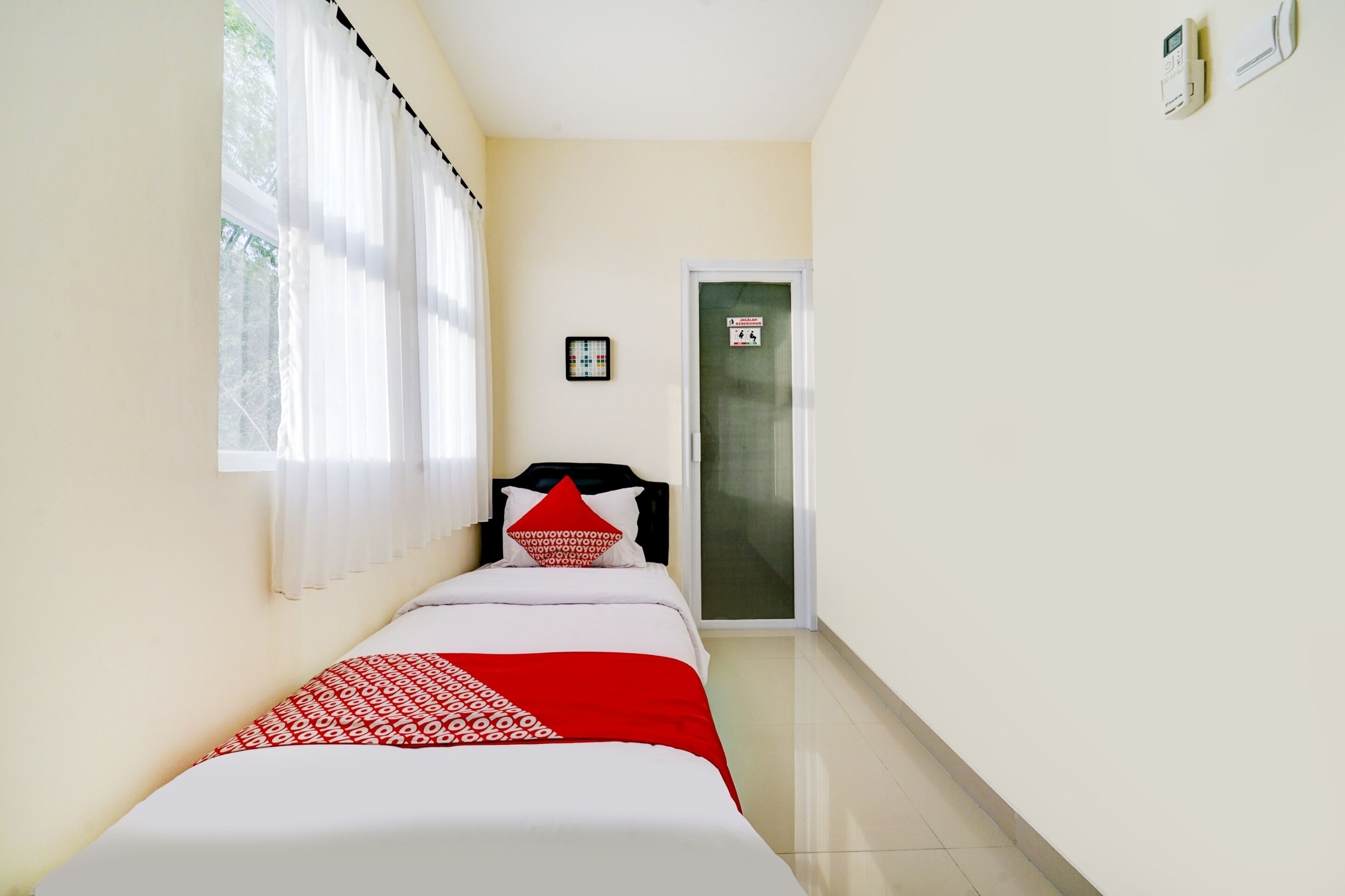 A narrow hallway with a bed at the end, a door with a sign, and a thermostat on the wall.