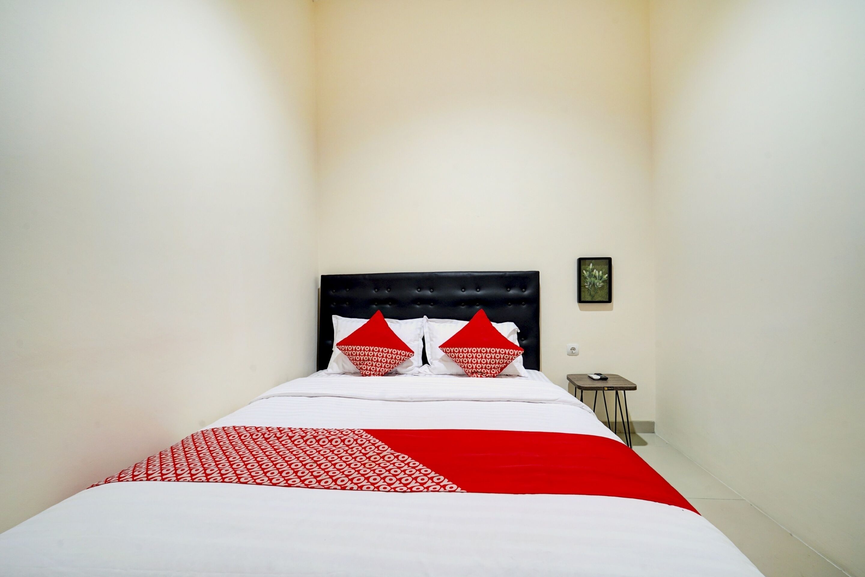 Een smalle hotelkamer met een bed, een klein nachtkastje en een ingelijst schilderij aan de muur.
